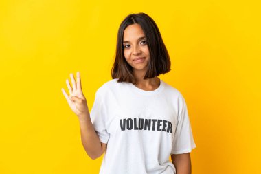 Sarı arka planda izole edilmiş genç gönüllü kadın mutlu ve parmakları olan dört kişi sayıyor.