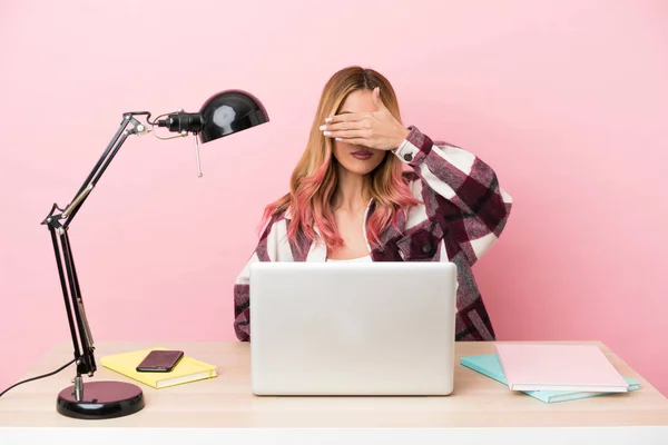 Young student woman in a workplace with a laptop over pink background covering eyes by hands. Do not want to see something