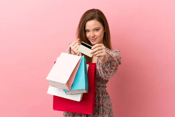 一个带着购物袋和信用卡的年轻姑娘 她的背景是孤立的粉色 — 图库照片