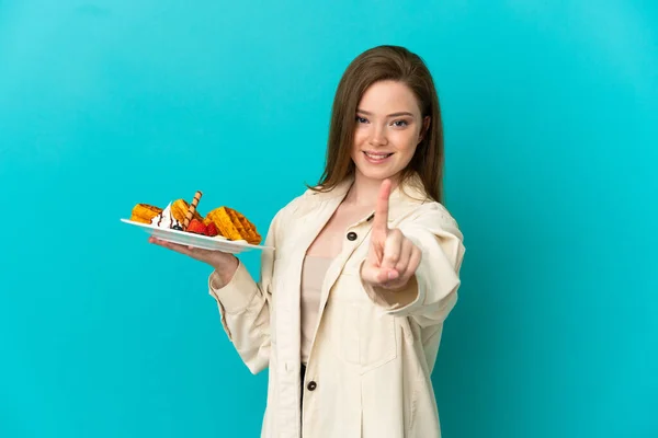 Adolescente Menina Segurando Waffles Sobre Isolado Fundo Azul Mostrando Levantando — Fotografia de Stock