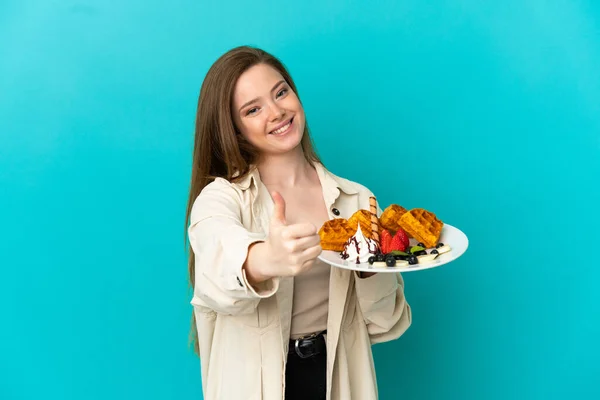 Adolescente Menina Segurando Waffles Sobre Fundo Azul Isolado Com Polegares — Fotografia de Stock