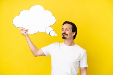 Sarı arka planda izole edilmiş genç beyaz bir adam düşünme balonu tutuyor.