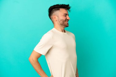 Genç beyaz adam mavi arka planda izole edildi. Çaba sarfettiği için sırt ağrısı çekiyor.