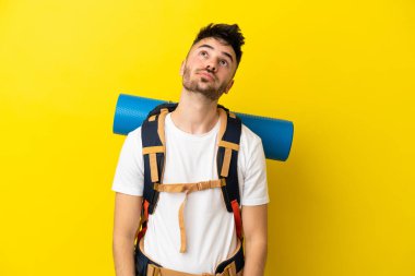 Sarı arka planda izole edilmiş büyük bir sırt çantası olan genç bir beyaz adam...