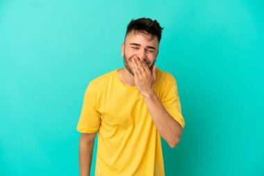 Mavi arka planda izole edilmiş genç beyaz adam mutlu ve gülümsüyor.