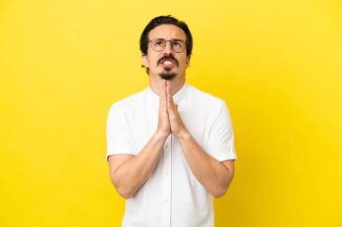 Sarı arka planda izole edilmiş genç beyaz adam avuç içlerini bir arada tutuyor. İnsan bir şey ister.