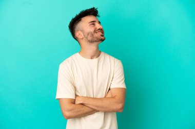 Genç beyaz adam mavi arka planda izole edilmiş gülümserken yukarı bakıyor.