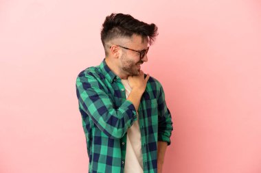 Genç, beyaz bir adam pembe arka planda izole edilmiş. Omuz ağrısı çekiyor. Çabaladığı için.