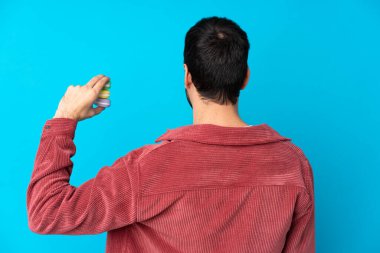 İzole edilmiş mavi arka planda genç beyaz adam renkli Fransız badem kurabiyelerini arka planda tutuyor.