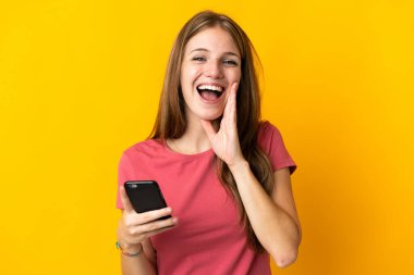 Sarı arka planda cep telefonu kullanan genç bir kadın ağzı açık bağırıyor.