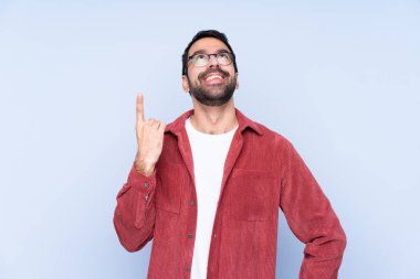 Mavi arka planda kadife ceket giyen genç beyaz adam yukarı bakıyor ve şaşırıyor.