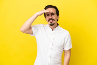 Kafkasyalı genç adam sarı arka planda izole edilmiş. Bir şeye bakmak için uzaklara bakıyor.