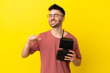 Elinde uzaktan kumandayla gezen adam sarı arka planda kendini beğenmiş ve gururlu.