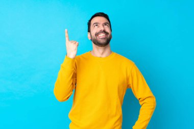 İzole edilmiş mavi arka planda genç beyaz adam yukarı bakıyor ve şaşırıyor.