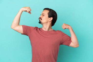 Mavi arka planda izole genç beyaz adam güçlü bir jest yapıyor.