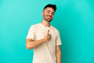 Kafkasyalı genç adam mavi arka planda izole edilmiş bir şekilde baş parmak işareti yapıyor.