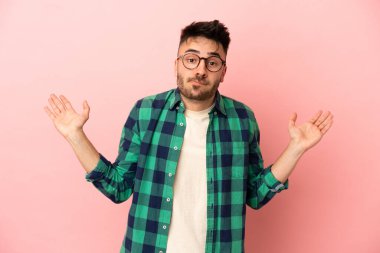 Pembe arka planda izole edilmiş genç beyaz adam ellerini kaldırırken şüpheleri var.