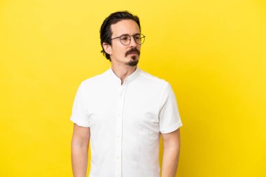 Sarı arka planda izole edilmiş genç beyaz adam yan tarafa bakıyor.