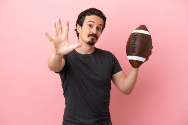 Pembe arka planda ragbi oynayan genç beyaz adam parmaklarıyla beşe kadar sayıyor.