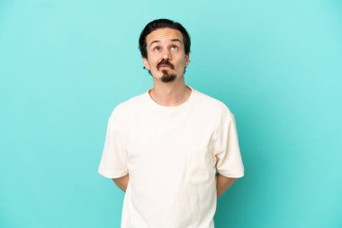 Kafkasyalı genç adam mavi arka planda izole edilmiş ve yukarı bakıyor.