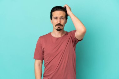 Kafkasyalı genç adam mavi arka planda izole edilmiş, hayal kırıklığı ifadesi var ve anlamıyor.