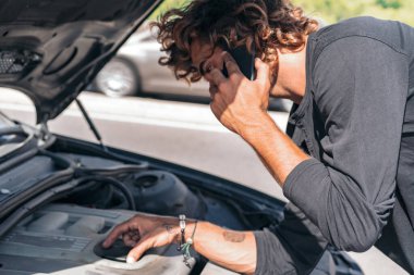 Genç beyaz bir adam arabasındaki arızayı düzeltmeye çalışıyor.