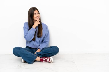 Genç bir kadın yerde oturuyor, yan tarafa bakıyor.