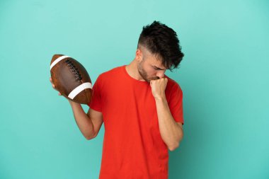 Rugby oynayan Kafkasyalı genç adam mavi arka planda izole edilmiş. Şüpheleri var.