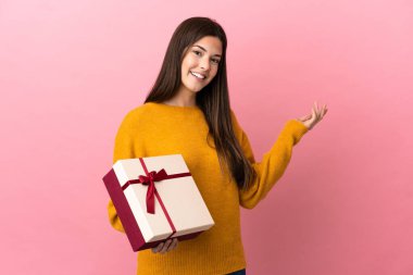 İzole edilmiş pembe arka plan üzerinde bir hediye tutan Brezilyalı genç kız, davet edildiği için ellerini yana uzatıyor.