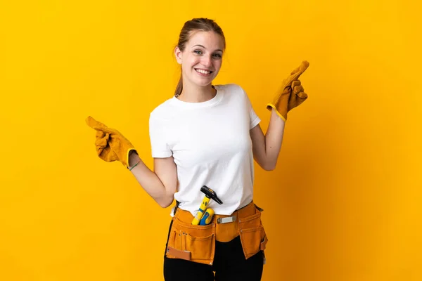 Young electrician woman isolated on yellow background pointing finger to the laterals and happy