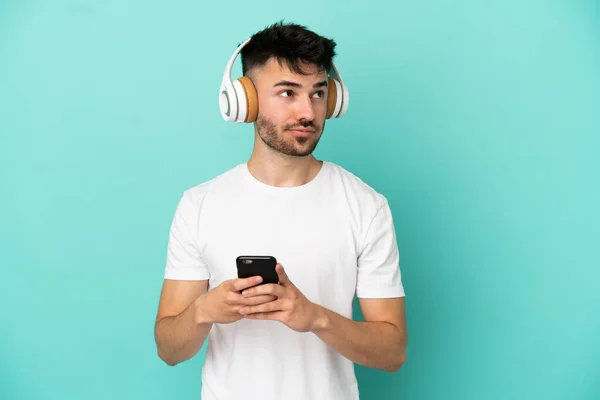 Joven Hombre Caucásico Aislado Sobre Fondo Azul Escuchando Música Con — Foto de Stock