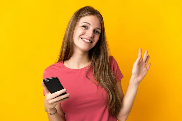 Mujer Joven Usando Teléfono Móvil Aislado Sobre Fondo Amarillo Saludando —  Fotos de Stock