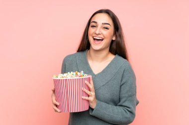 Pembe arka planda izole edilmiş beyaz bir kadın elinde koca bir kova patlamış mısır tutuyor.