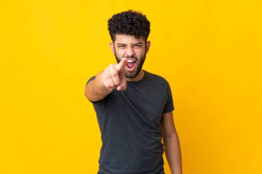 Faslı genç adam sarı arka planda izole edilmiş hayal kırıklığına uğramış ve ön tarafı işaret ediyor.