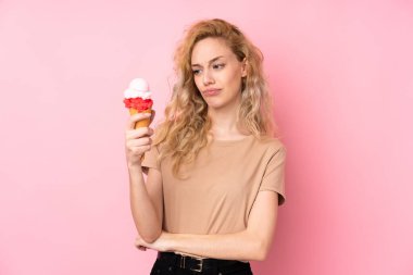 Kornet dondurması tutan genç sarışın kadın üzgün bir ifadeyle pembe arka planda izole edilmiş.