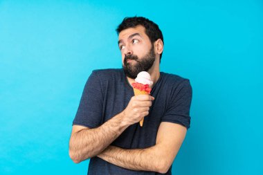 Kornet dondurması ile izole edilmiş mavi arka planda kalan genç adam omuzlarını kaldırırken şüpheyle hareket ediyor.