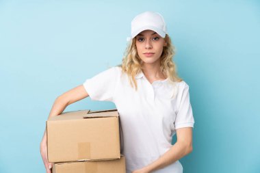 Mavi arka planda izole edilmiş, kollarını kavuşturan genç teslimatçı kadın.