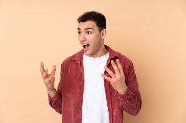 Beyaz tenli yakışıklı adam, bej arka planda izole edilmiş, şaşırmış bir yüz ifadesi var.