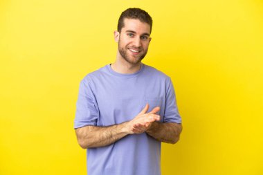 Sarışın yakışıklı adam izole edilmiş sarı arka plan alkışlıyor.