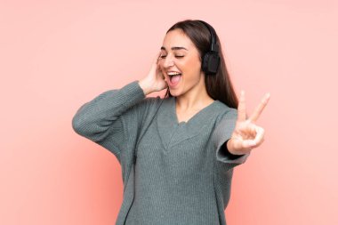 Genç beyaz kadın pembe arka planda izole edilmiş müzik dinliyor ve şarkı söylüyor.