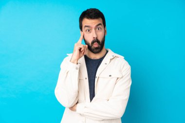 Beyaz kadife ceketli genç yakışıklı bir adam izole edilmiş mavi arka planda bir fikir düşünüyor.