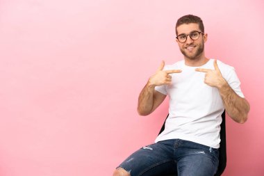 İzole edilmiş pembe arka planda oturan genç adam gururlu ve kendini beğenmiş.