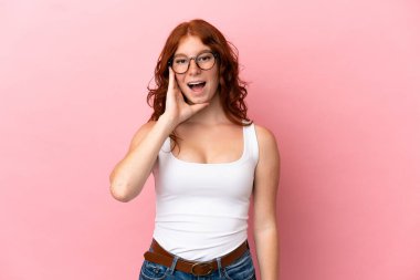 Genç kızılımsı kadın pembe arka planda izole edilmiş, şaşırmış ve şok olmuş bir yüz ifadesi var.
