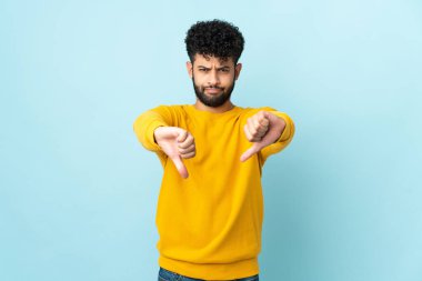 Mavi arka planda izole edilmiş genç Faslı iki eliyle baş parmağını gösteriyor.