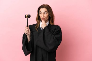 Orta yaşlı yargıç kadın pembe arka planda izole edilmiş, yana bakıyor ve gülümsüyor.