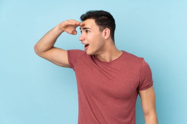 Beyaz tenli yakışıklı adam mavi arka planda izole edilmiş. Bir şeye bakmak için uzaklara bakıyor.