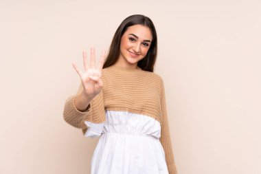 Beyaz tenli genç bir kadın bej arka planda izole edilmiş mutlu ve parmaklarıyla dört kişi sayıyor.