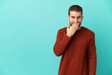 Sarışın yakışıklı, soyutlanmış mavi arka planda mutlu ve gülümseyen, ağzı kapalı bir adam.