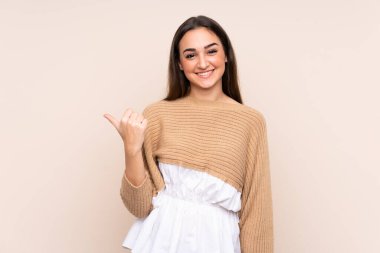 Beyazlı genç bir kadın bej arka planda izole edilmiş bir şekilde bir ürün sunmak için kenarı işaret ediyor.