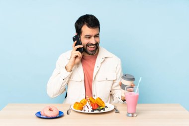 Masada waffle yiyen ve milkshake içen bir adam cep telefonuyla sohbet ediyor.